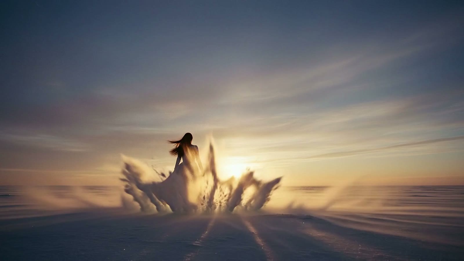 Sunrise breaking across a frozen plain, ice lifting in the wind around a small figure.